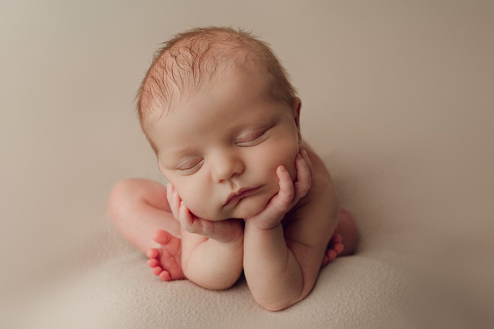 A newborn baby rests its sleeping head on its hands