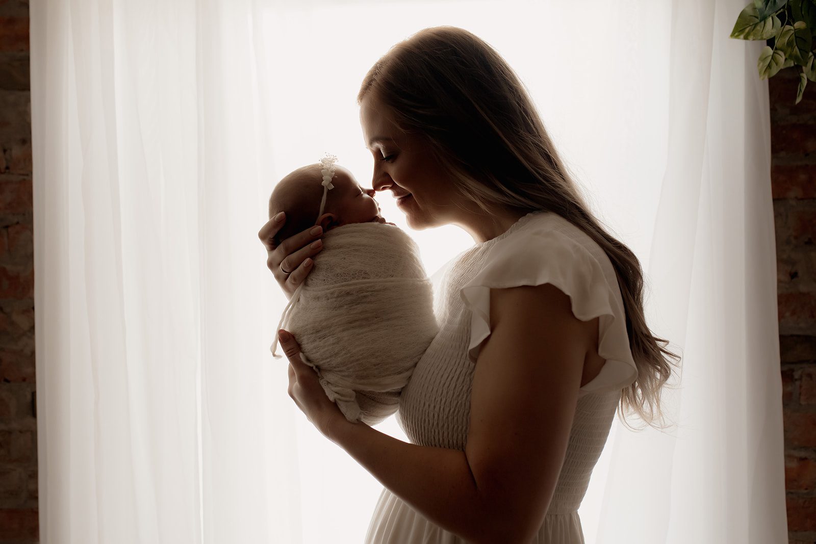 Silhouette of a mom nuzzling her sleeping newborn baby in a window after using Beautiful birth choices