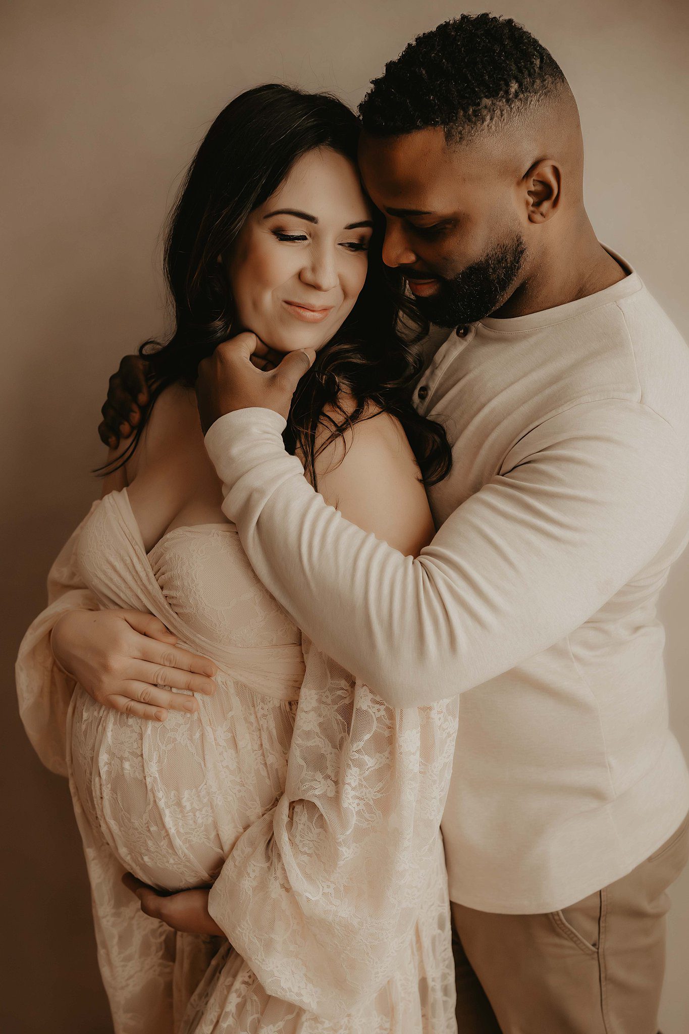 A happy expecting couple snuggle in a studio while holding the bump