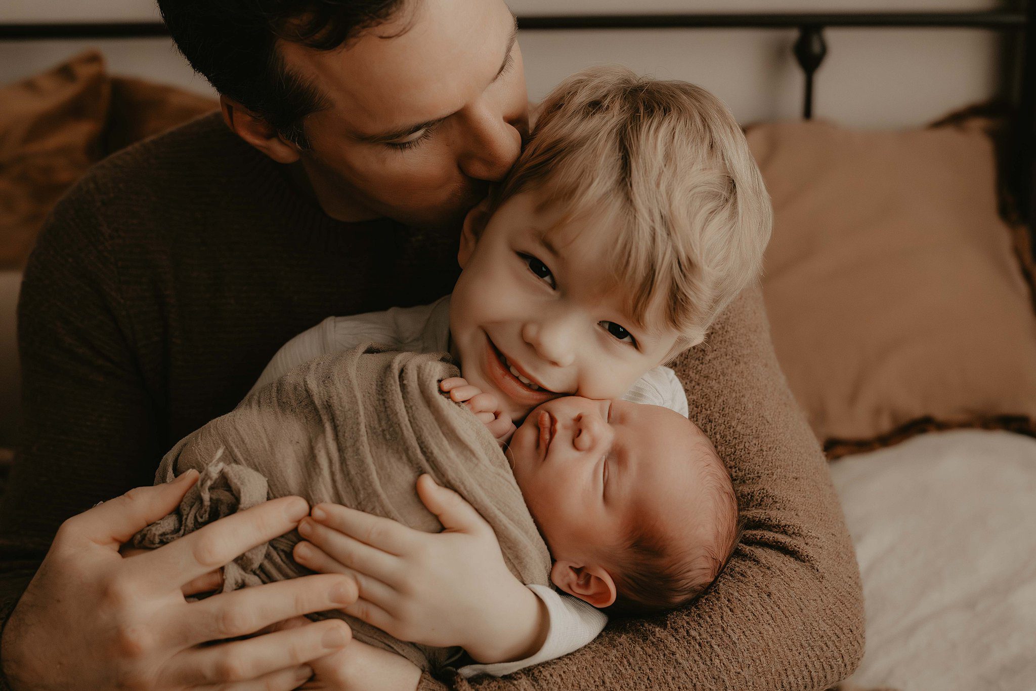 A newborn baby sleeps while being cuddled by dad and older brother