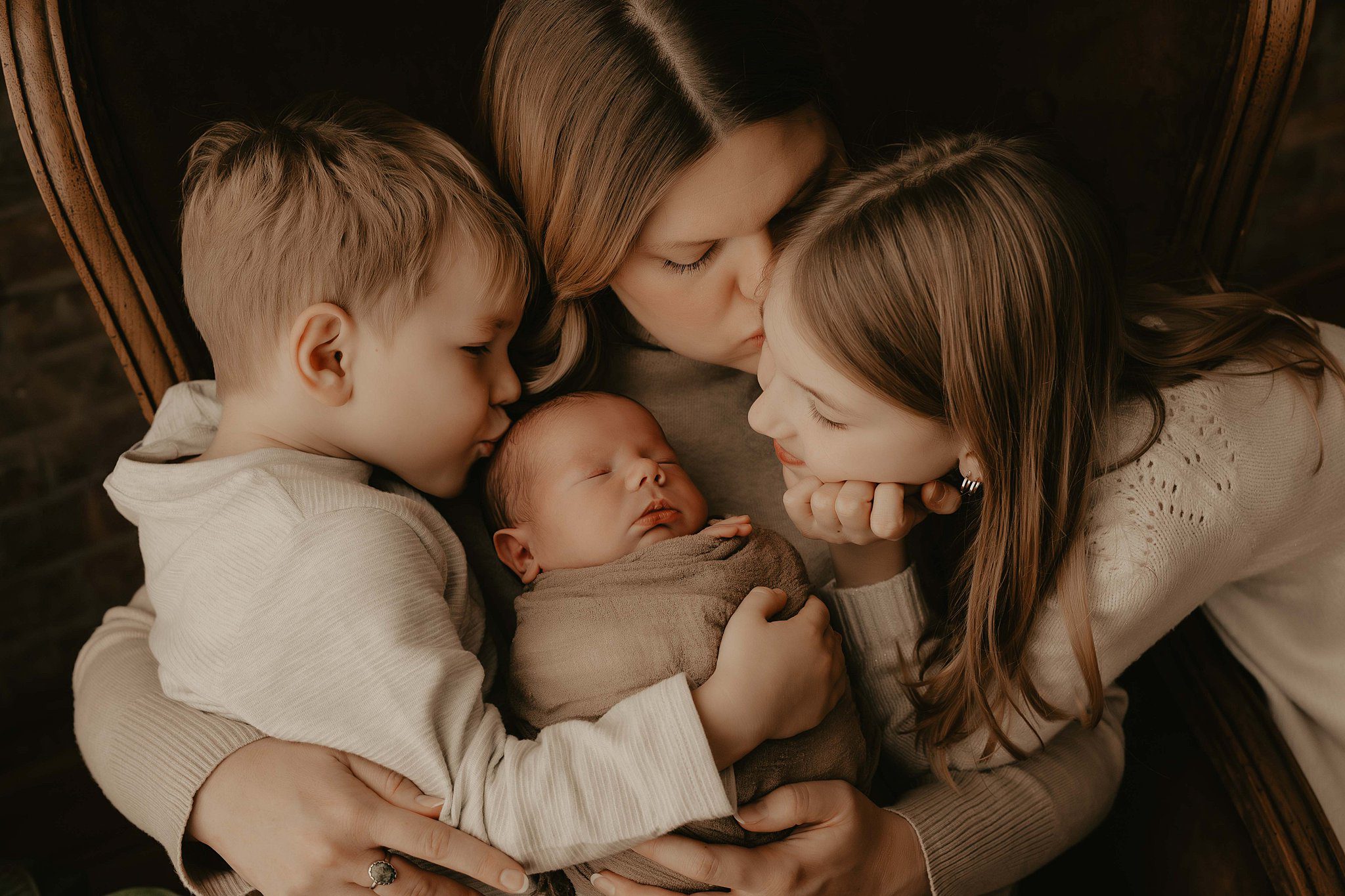 A newborn baby sleeps on mom's chest while her toddler son and daughter kiss and admire the baby after meeting a doula in Rochester, NY