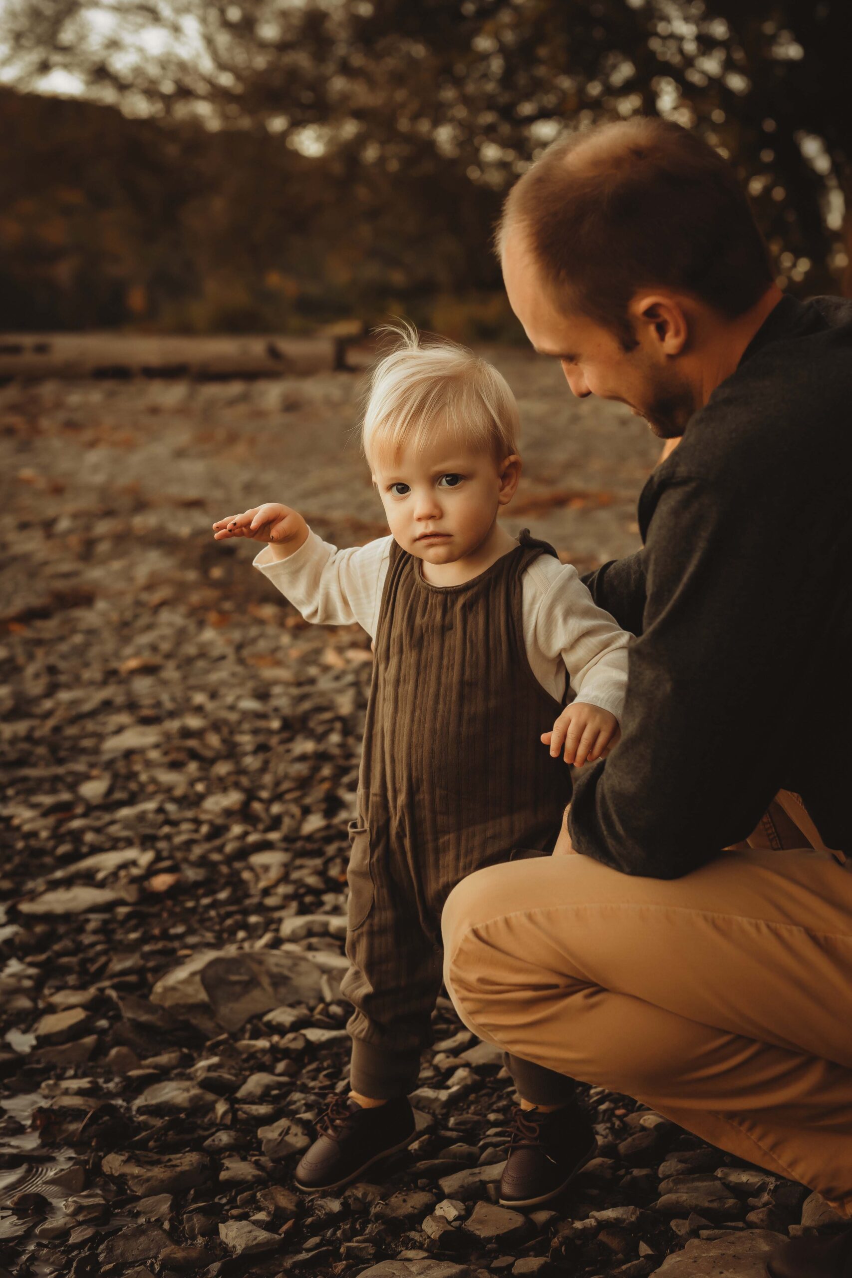 A young boy walks in a park with dad's help in brown overalls after meeting nannies in rochester, ny